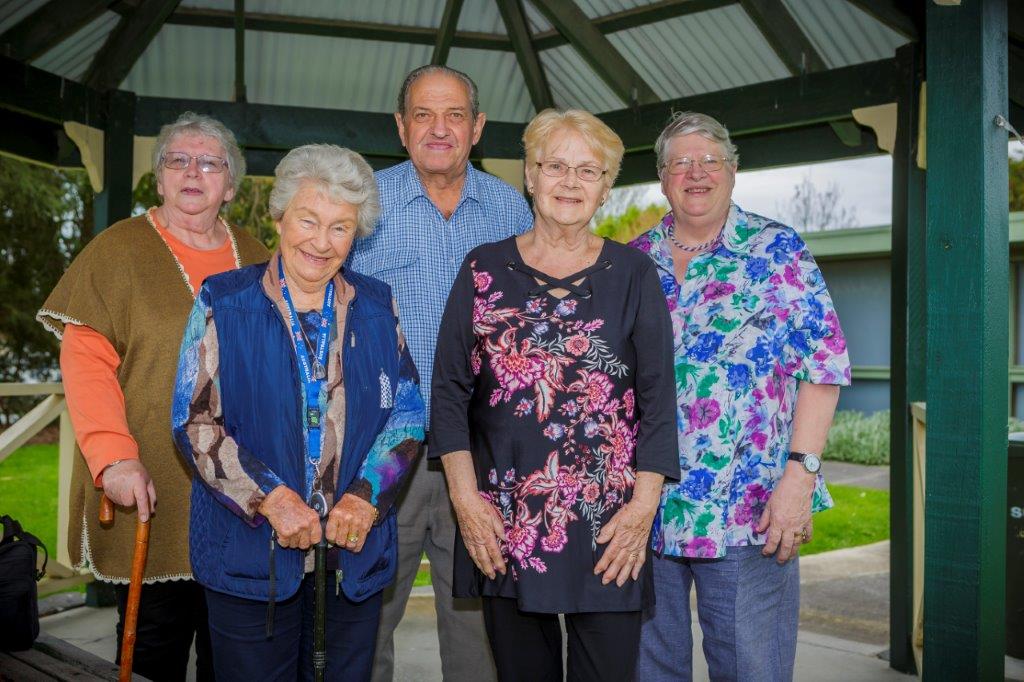 A group of seniors standing under a pergola in a park